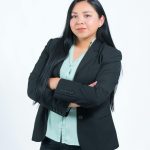 Confident businesswoman in a formal attire standing with arms crossed against a plain background.